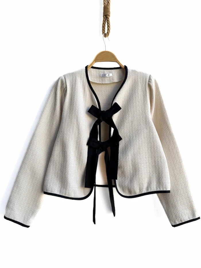 Chaqueta corta marfil con lazos y bordes negros.